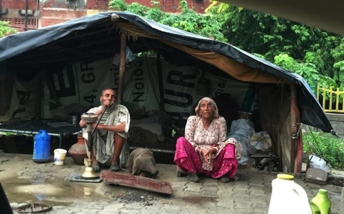Una pareja de personas mayores sentada frente a su “casa”, una estructura hecha con bolsas de plástico y materiales de desechos. Crédito: Neeta Lal/IPS