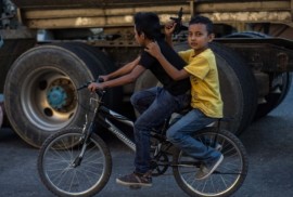 Dos niños transitan en una bicicleta por una calle del centro de Ciudad de Guatemala, el pasajero con una pistola de juguete en sus manos. Las armas son parte cotidiana en las urbes de este país centroamericano. Crédito: Ximena Natera/Pie de Página