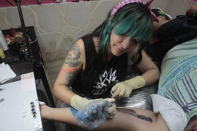 La tatuadora Ana Lyem Lara mientras grababa la imagen de un cuchillo en la piel de un cliente, en su estudio casero Zenit, en el sector costero de Santa Fe, en el municipio de Playa, en La Habana. Las mujeres aumentan su presencia en este arte en Cuba. Crédito: Jorge Luis Baños/IPS