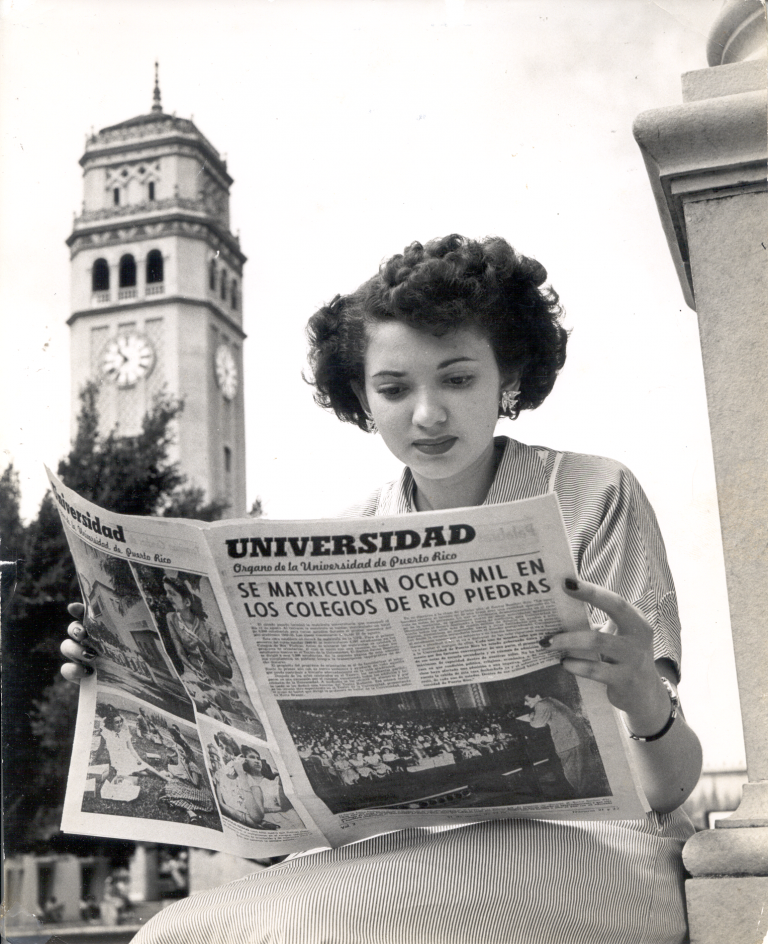 Estudiante lee periódico frente a la Torre del Recinto de Río Piedras